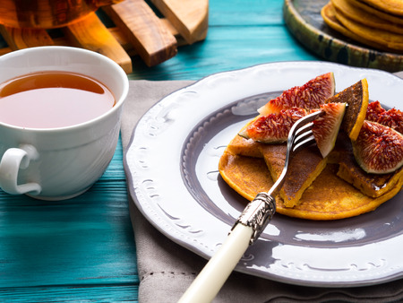 Eating pumpkin pancakes with figs and honey with hot tea. Autumn food background on green wooden tableの写真素材