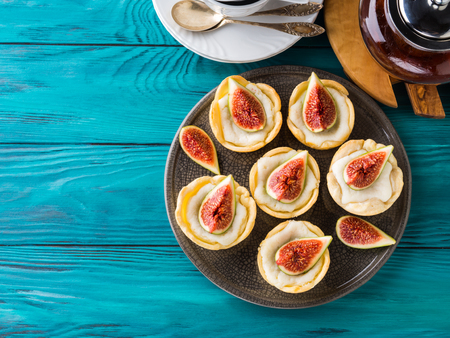 Tartlets with ricotta and figs on green wooden table. Mini treats