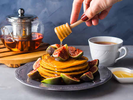 Stack of pumpkin pancakes with figs and honey and hot tea. Autumn food background on blue gray backdropの写真素材