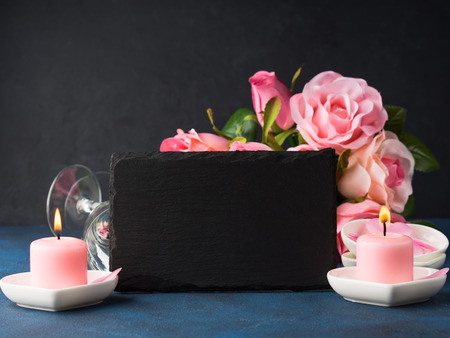 Valentine's day concept and greeting card. Romantic date invitation with pink candles, roses, hearts and black board for writing greetingsの写真素材