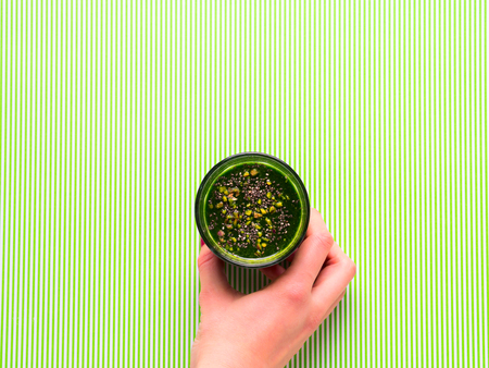 Healthy Green smoothie with spinach, cucumber, spirulina, apple and chia seeds. Woman's hand holding...