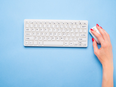 White keyboard and womans hand on mouse. Blue minimal background