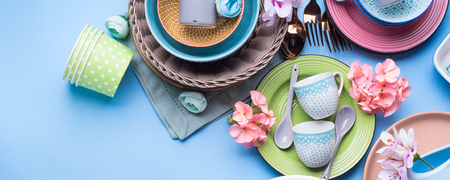 Tableware dish set on blue pastel background with flowers. Flat lay