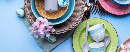 Tableware dish set on blue pastel background with flowers. Flat lay