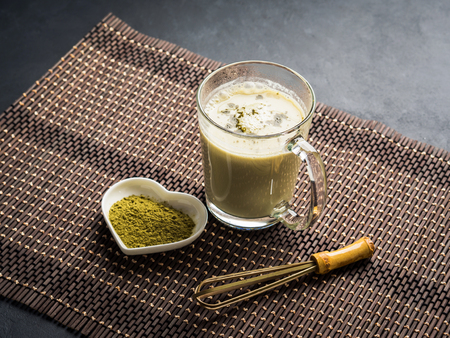 Green matcha tea latte mug on dark background with powder and whisk