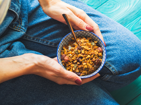Girl wearing jeans eating home made granola bowl with yogurt for breakfast. Pumpkin pie granola with...