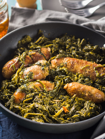 Italian sausages with rapini broccoli in a skillet with table setting on green wooden tableの写真素材