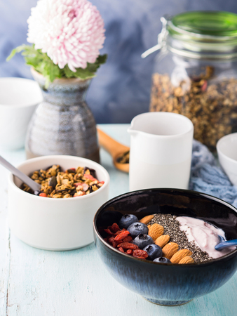 Yogurt raspberry smoothie bowl with goji berries and blueberries, almonds, chia seeds and granola on pastel turquoise wooden background. Plant based breakfastの写真素材