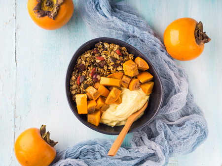 Golden turmeric yogurt smoothie bowl with persimmon and matcha granola on pastel turquoise wooden background. Plant based vegan breakfastの写真素材