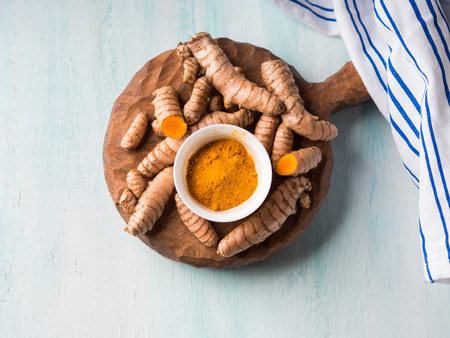 Turmeric spice in powder and roots on wooden boardの写真素材