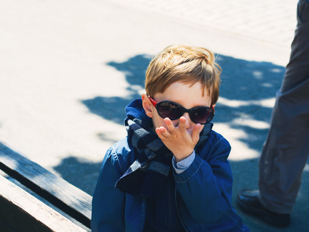 Little funny blonde 5-year-old boy outdoors with funny sun glasses. Boy sending a kiss with hand