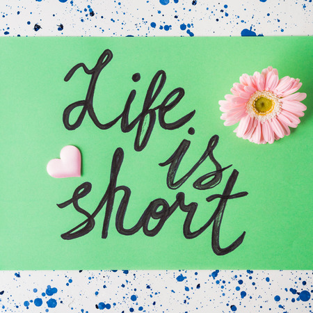 Life is short quote written on green sheet on pastel green background with flowersの写真素材