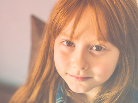 Cute redhead little girl looking at the viewer and smiling. Vivid eyes and cheerful smile. Toned