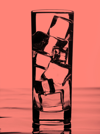 Glass of water with ice cubes. Pink coral tonedの写真素材