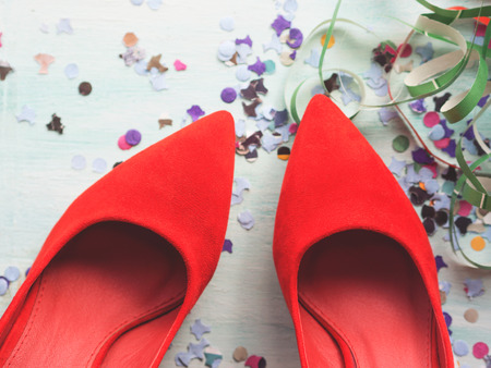 Party flat lay background with womans red shoes, colorful confetti, streamers