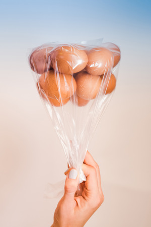 Eggs in plastic bag upside down as balloons in womans hand on multi color blue and light coral pink background with soft lightの写真素材