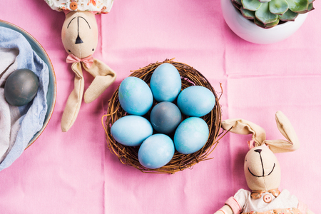 Pink easter holiday concept with bunnies and blue colored hard boiled eggs in a basket. Table decor flat layの写真素材
