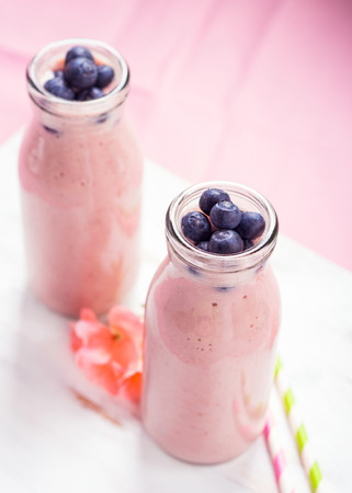 Pink milk shake in glass bottles topped with blueberries. Pink flowers and colorful straws.の写真素材