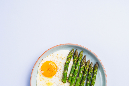 Fried eggs with steamed asparagus flat lay on blue gray background. Delicious healthy lunch. Keto dietの写真素材