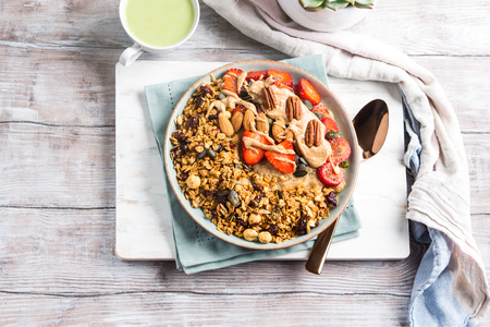Delicious amaranth porridge topped with home made granola, strawberries and almond butter. Vegan plant based breakfast served with matcha latte on white wooden board. Healthy colorful food conceptの写真素材