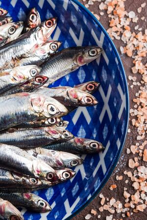 Blue fish. Fresh anchovies in a dish with pink salt on dark brown background. Healthy protein meal. Local seafood, Italyの写真素材
