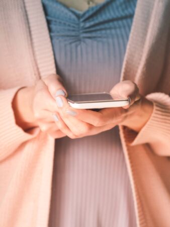 Woman using white smartphone. No face, closeup on hands with mobile phone. Pastel colorsの写真素材