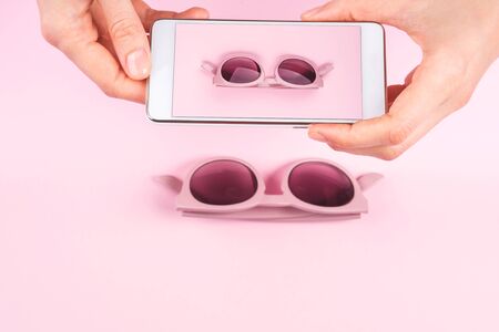 Woman taking picture of pink sunglasses with smatphone. Abstract fashion technology conceptの写真素材