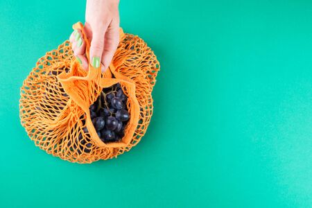 Zero waste concept. Reusable mesh shopping bag full of fresh fruit being held by womans hand with green manicure. Plastic free lifestyle copy spaceの写真素材