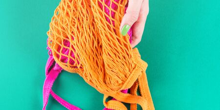 Zero waste concept. Color mesh shopping bags on green. Flat lay with hands with green manicure on nailsの写真素材