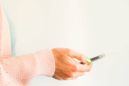 Young woman wearing pastel pink and green mint clothes using mobile phone. Closeup on hand. Copy...