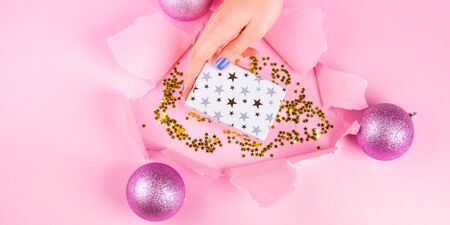 Festive pink background with paper hole and golden confetti. Female hand taking gift boxの写真素材