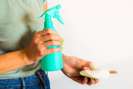 Woman wearing green t-shirt holding reusable cotton pads, wooden comb and spray bottle with home...