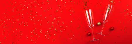 Two champagne glasses with golden star shaped confetti on red color background. Celebrating new year, christmas, valentines day concept festive flat lay. Long website bannerの写真素材