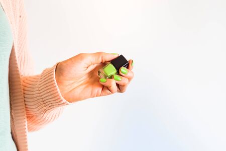 Woman holding green mint nail polish bottle of same color of the manicure in hand. White background copy space. Beauty concept, pastel colorsの写真素材