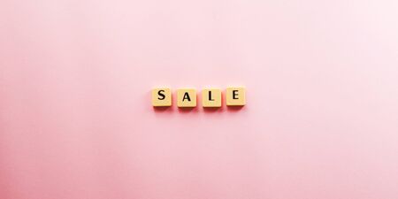 Sale word composed with plastic tiles on pink background. Discount period concept flat lay