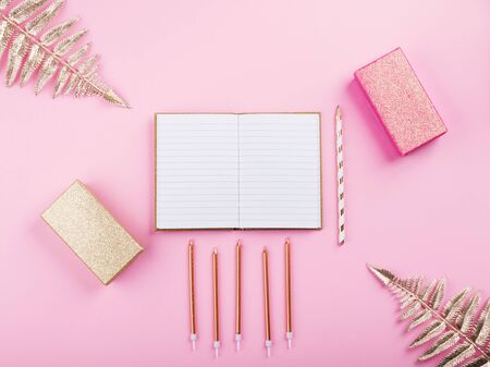 Golden tropical plant branches frame and open notebook on white pages with pen, glitter gifts, candles on pink millennial backdrop. Trendy flat lay and mock up for writing. Happy birthday, anniversaryの写真素材