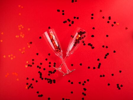 Happy valentines day concept flat lay with champagne flutes and red heart confetti on red background.の写真素材