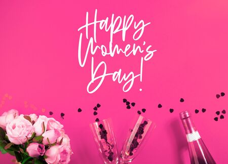 Happy womens day pink flat lay card with champagne, heart confetti, rose flowers and champagne flutes and bottle. Greeting card with textの写真素材
