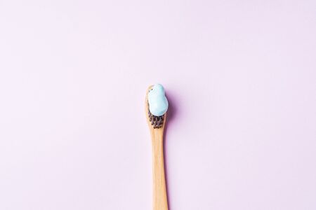Bamboo toothbrush with blue toothpaste on pink lilac background. Personal dental hygiene concept....