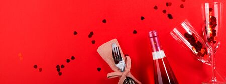 Romantic dinner concept flat lay web banner on red background with, festive napkin tableware and champagne flutes and bottle. Greeting card, invitation mockup with heart confettiの写真素材