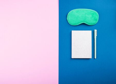 Sleeping mask and sleep journal with pen on classic blue and pink background. Better sleep concept.
