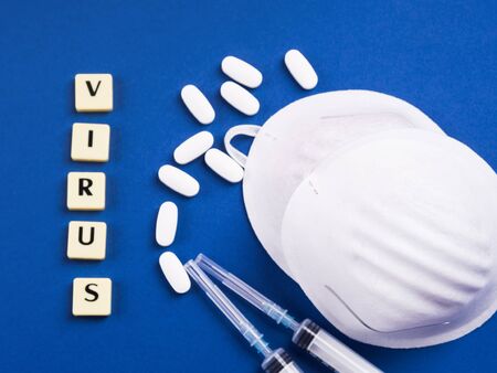 Viral disease treatment and prevention concept. Epidemic danger prevention. Treatment concept with masks, syringes and antibiotic pills on blue backgroundの写真素材
