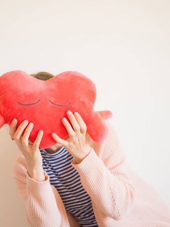 Faceless woman covering her face with red heart shaped plush toy.の写真素材