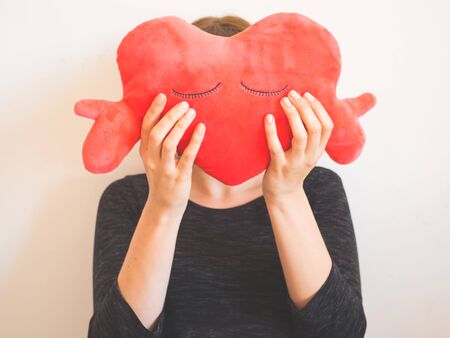 Faceless woman covering her face with red heart shaped plush toy.の写真素材
