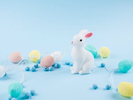Easter bunny with colorful eggs shaped lights string on blue background, copy space