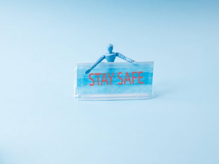 Covid-19 coronavirus pandemic concept with wooden marionette holding medical face mask with text message Stay home and stay safe on blue backgroundの写真素材