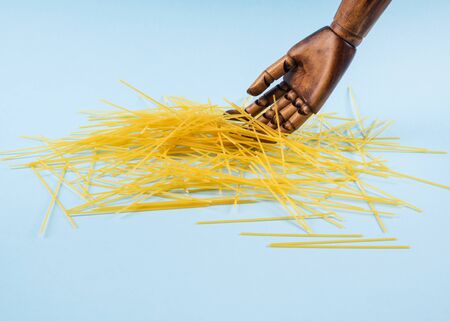 Concept of economic crisis in Italy due to Covid-19 pandemic with large wooden hand touching broken spaghetti over abstract blue backgroundの写真素材