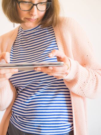 Smiling young woman with eyeglasses and brown hair wearing pastel color clothes using tablet. Study, work from home conceptの写真素材
