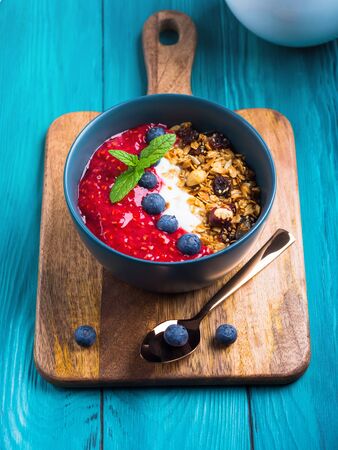 Yogurt smoothie bowl with blended raspberries, blueberries and oat matcha granola on dark green wooden background. Delicious healthy breakfast conceptの写真素材