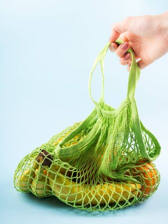 Green mesh shopping bag with bananas, kiwi and oranges. Colorful fresh organic fruit. Zero waste concept - plastic free reusable cotton bag held by female handの写真素材